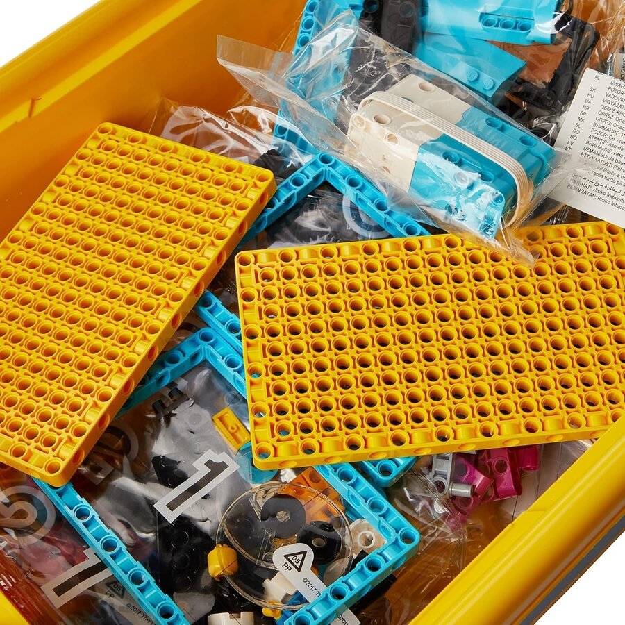 Kit LEGO® SPIKE™ Prime recién abierto: caja amarilla con bases perforadas, vigas Technic azules, el hub programable en su bolsa y bolsas numeradas de piezas.